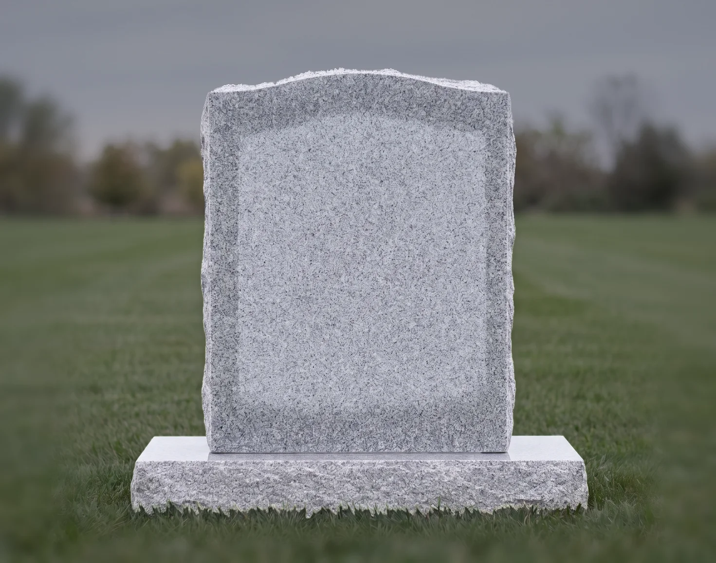 A grey granite single upright headstone, blank, on a lawn